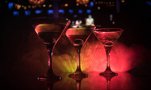 几杯著名的鸡尾酒马提尼, 拍摄在酒吧与黑暗色调的雾背景和迪斯科灯。俱乐部饮料的概念。选择性聚焦