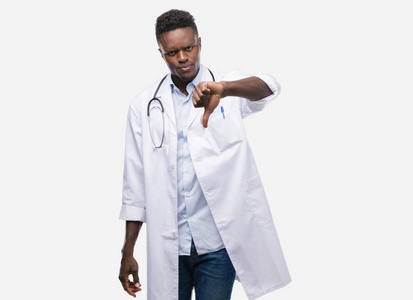年轻的非洲裔美国人穿着医生外套与愤怒的面孔, 消极标志显示不喜欢与拇指下来, 拒绝概念