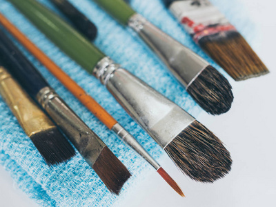 一排艺术家画笔在白色背景复古风格的蓝毛巾上隔离