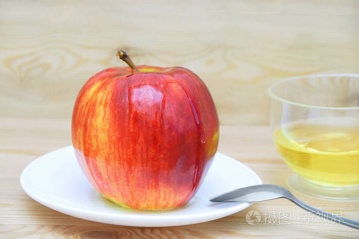 苹果在一个白色的盘子里, 用勺子把蜂蜜放在木质的背景上.