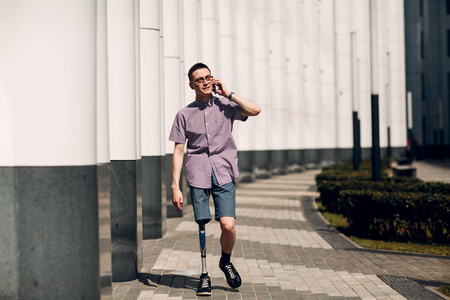 持有的脚残疾的年轻人用脚假肢沿着街道走, 并持有手机照片