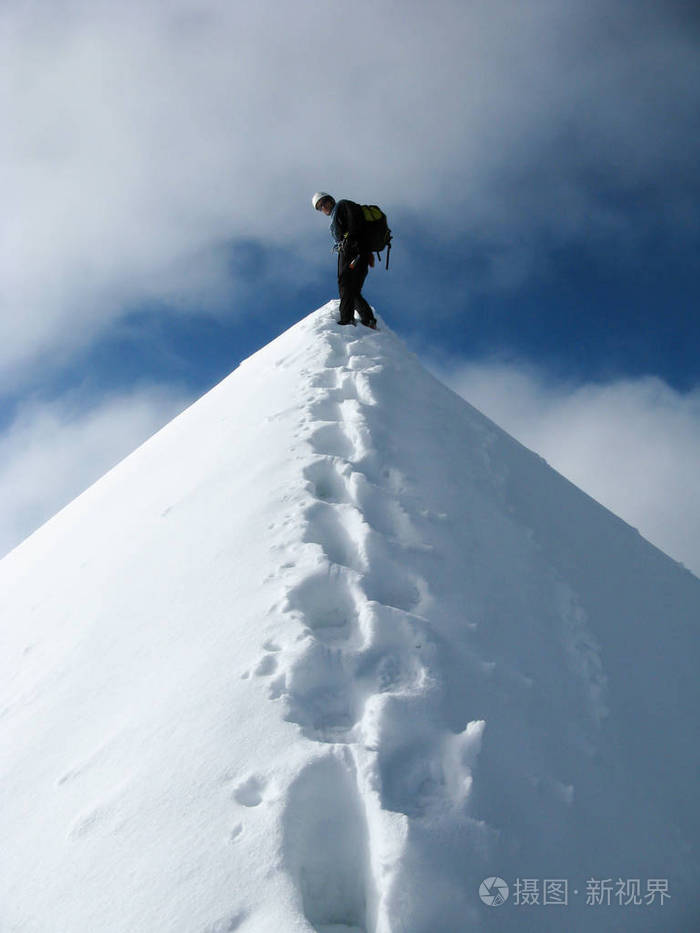 登山者站在高一个狭窄和暴露的雪山峰与轨道领先