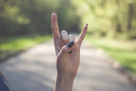 撒旦女孩做在阳光明媚的绿色背景下的角手势的标志 撒旦的手指照片