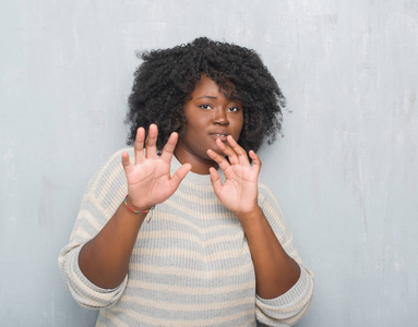 年轻的非洲裔美国人加上大小的女人在灰色的垃圾墙穿着一件毛衣害怕和恐惧的表情停止手势, 在震惊中大叫。恐慌概念