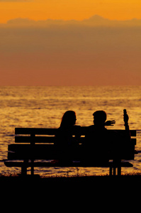 嬉戏的年轻夫妇坐在长凳上日落