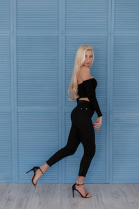 穿着时髦的黑色衣服的漂亮年轻女子在一堵老式的蓝色木墙附近摆姿势