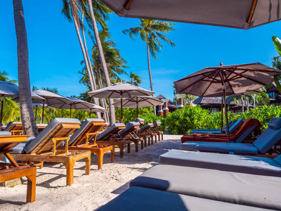 海滩和海洋上的雨伞和椅子, 周围有蓝天, 椰子棕榈树, 用于旅行和度假