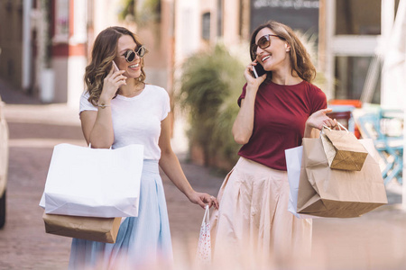 两个女人走在历史悠久的城市中心与购物袋和在手机上说话。意大利购物概念