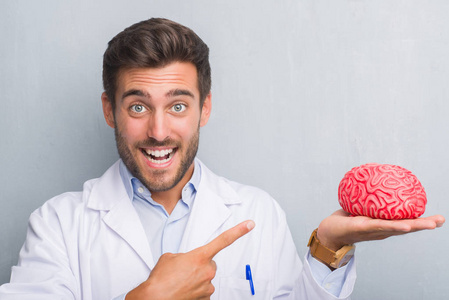 英俊的年轻医生心理学家男子在灰色的格格墙举行着一个大脑非常高兴地指着手和手指