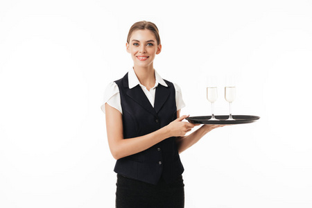 漂亮的托盘年轻漂亮的女服务员在制服举行托盘与眼镜高兴地看着在白色