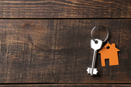 买房的概念。钥匙与钥匙串房子在棕色木制背景。从上面的意见。有刻字空间