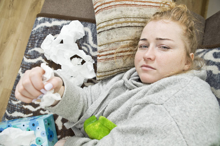 头痛和流感的年轻女子躺在家里的沙发上。休闲风格的室内拍摄