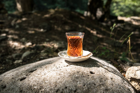 在森林的石头上玻璃上的东方红茶。东方茶的概念。Armudu 传统杯。绿色自然背景。选择性聚焦