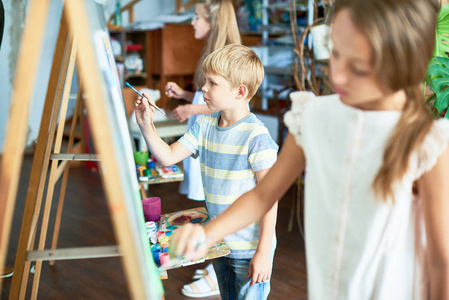 在艺术课工作室里, 一群孩子在画架上画画, 他们的侧视图相当关注小男孩