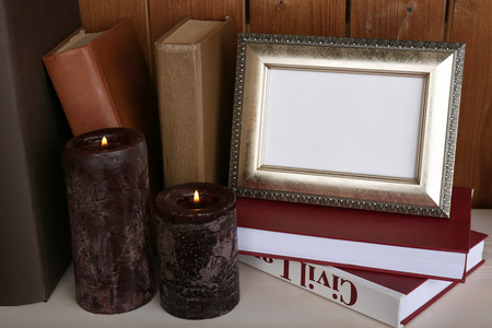 相框用蜡烛和木制表面和木墙背景上的书