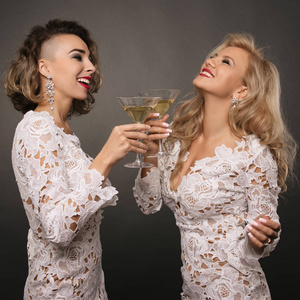 两个美丽的年轻女性女友在白色短裙庆祝节日与马提尼眼镜隔离