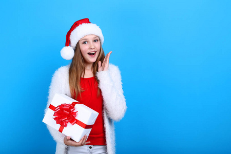 年轻的女孩在圣诞老人帽子举行礼物盒在蓝色背景