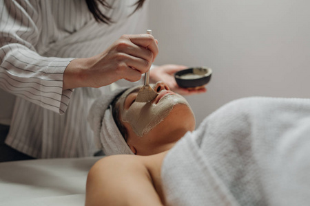 白人美容师妇女在一个美丽的年轻白种女人的脸上涂抹面部面具躺在按摩