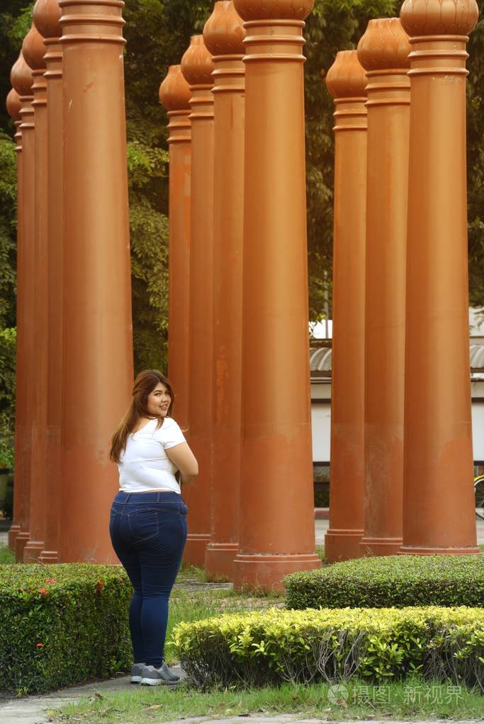 亚洲漂亮的笑脸脸胖女人姿势走路并持有一本小册子在公园的杆组