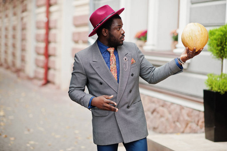 时尚的非洲裔美国人男子模型灰色夹克领带和红帽手持南瓜手