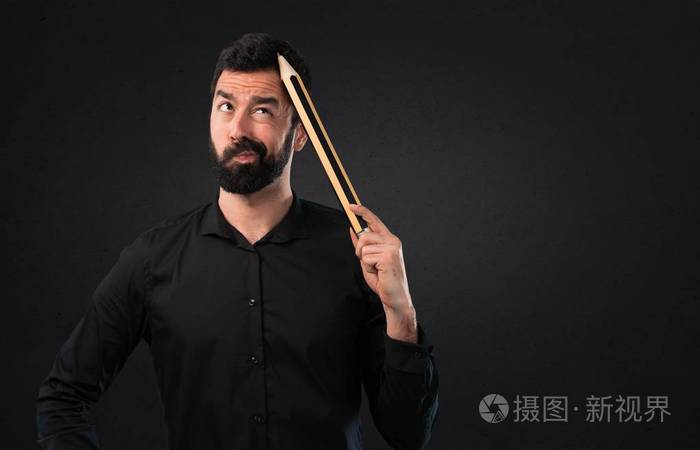 有胡子的英俊的人拿着一支大铅笔在黑色背景上