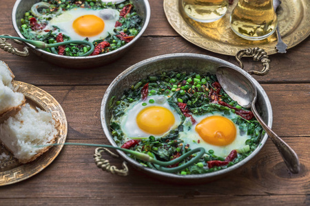 绿色 shakshuka。鲜菠菜煎蛋, ramson, 韭菜在灰色背景下的平底锅, 顶部视图