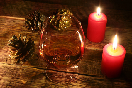 圣诞节蜡烛和玻璃与白兰地或威士忌在木材背景。圣诞装饰