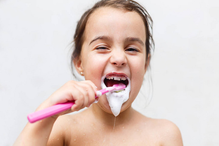 小女孩刷她的牙齿站在白色背景