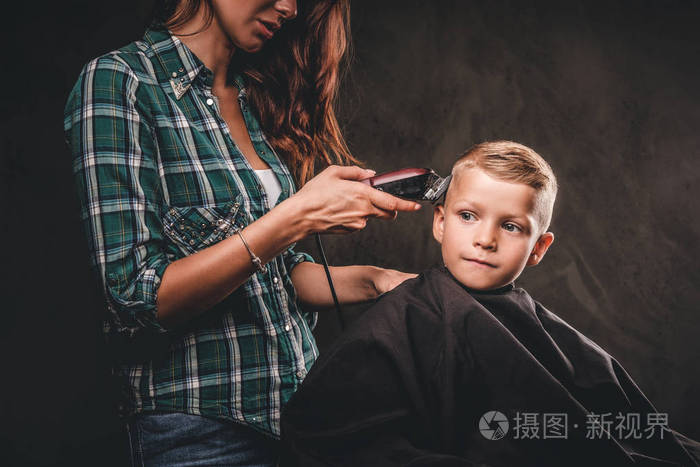 儿童理发师的修剪是削减小男孩对黑暗的背景可爱的学龄后男孩得到理发