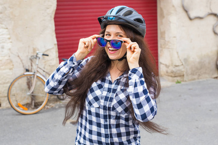 在背景自行车和红色门拿着太阳镜的年轻美丽的妇女