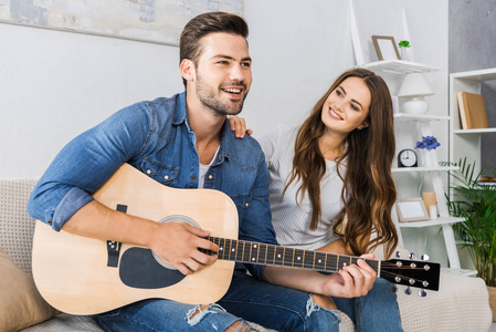 年轻幸福夫妇坐在沙发上与声学吉他在家里