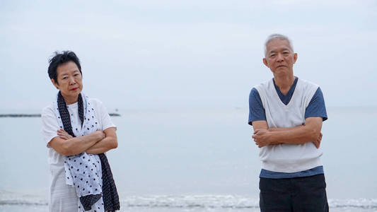 亚洲老年夫妇在海洋海滩上战斗不安