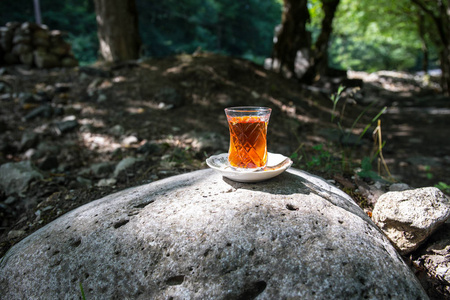 在森林的石头上玻璃上的东方红茶。东方茶的概念。Armudu 传统杯。绿色自然背景。选择性聚焦