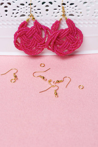 手工制作的珠子耳环。粉红色的颜色。坚持立场。附近是散耳线和其他配件。在家里做针线活。珠首饰