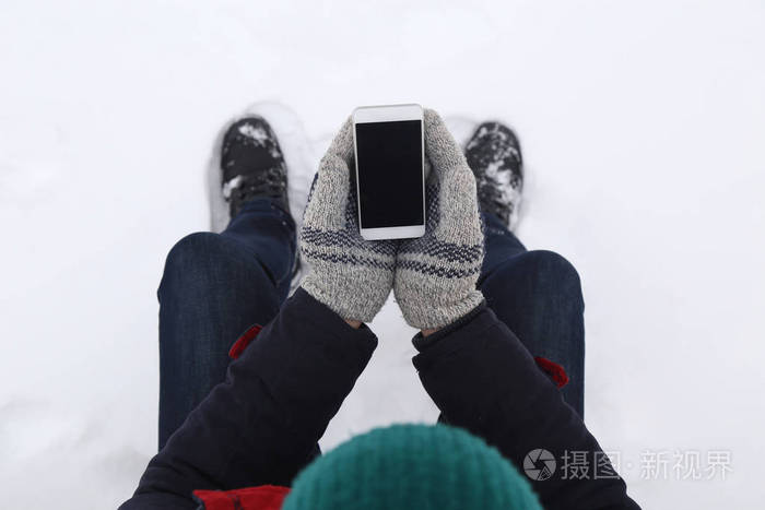 在雪地和手持空白屏幕智能手机的人的高角度视图