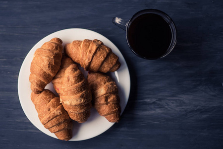 伙计穆迪的颜色。咖啡和新鲜的牛角面包在黑色的背景。甜点和咖啡。早餐的概念。宏快照