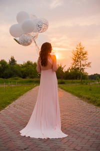 快乐美丽的女人在粉红色的长裙散步与空气气球在绿色公园在日出的夏天天图片