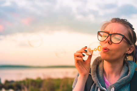 一个戴着眼镜在湖边吹肥皂泡的年轻女子的肖像