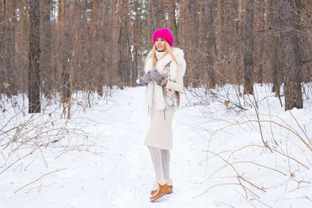 季节和人概念有吸引力的金发碧眼的妇女穿着白色外套和粉红色的帽子站在冬季雪景公园