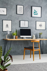 桌面上的海报画廊与台式计算机在灰色家庭办公室内部与椅子。真实照片