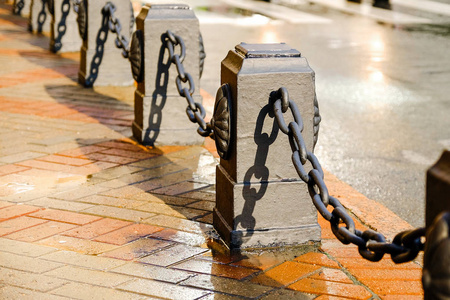 石栅栏有锁链的栅栏.道路背景中的铁链围栏.铺路石照片