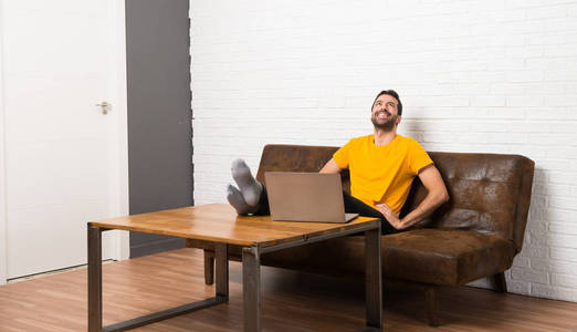 男人与他的笔记本电脑在一个房间摆姿势, 双臂在臀部和笑