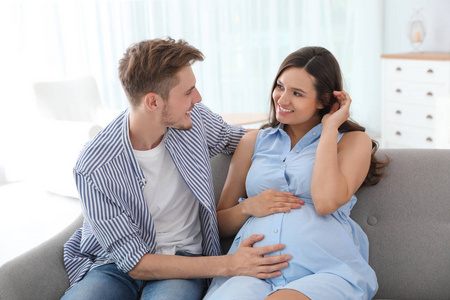 年轻人和怀孕的妻子坐在家里的沙发上
