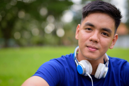 年轻英俊的亚洲男子戴着耳机在公园里放松