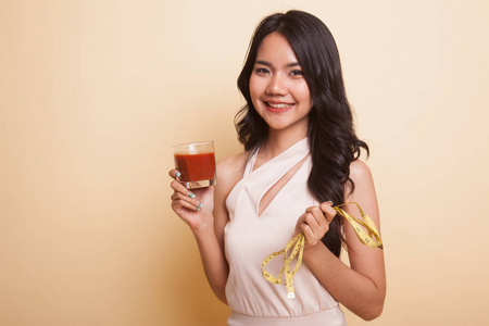 年轻的亚洲妇女与蕃茄汁和测量胶带在米色背景