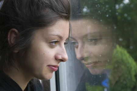 伤心的女孩从窗外看着雨。女人与漂亮的期待听到