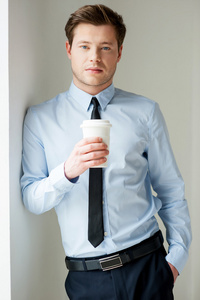 英俊的年轻男人的衬衫和领带捧着一杯咖啡