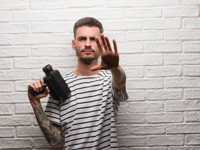 年轻人拍摄手持摄像机站在白色砖墙上用张开的手做停止标志以严肃和自信的表达, 防御姿态