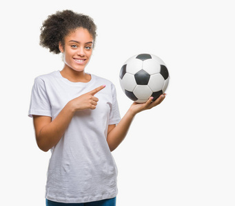 年轻美丽的美国黑人举行足球足球在孤立的背景很高兴指向用手和手指