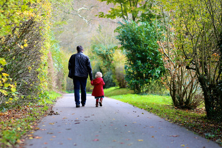 父亲大衣父亲带着小女儿在公园里一起散步照片